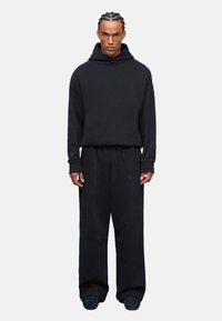 Sudadera negra de gran tamaño con un bolsillo canguro, combinada con pantalones de chándal negros de corte holgado, que presentan una textura suave y acentos mínimos.