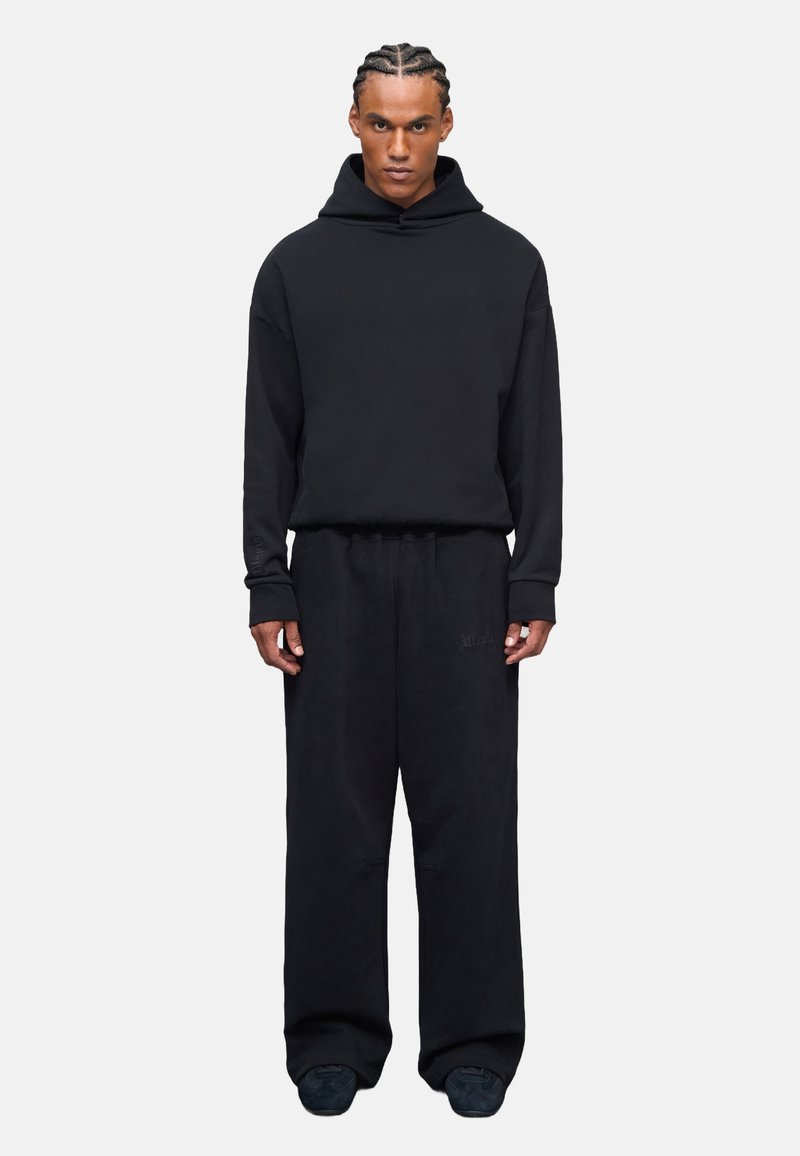Sudadera negra de gran tamaño con un bolsillo canguro, combinada con pantalones de chándal negros de corte holgado, que presentan una textura suave y acentos mínimos.
