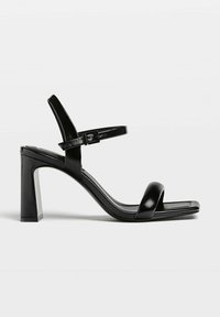 Sandales à talons hauts en cuir noir avec un bout carré, une bride réglable à la cheville et un talon bloc. Texture lisse et design minimaliste.