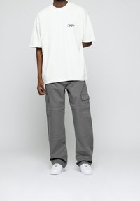Witte katoenen t-shirt met een klein groen logo, gecombineerd met grijze cargobroek met zijzakken en een relaxte pasvorm. Witte sneakers.