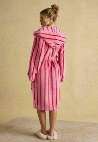 Różowy, pasiasty szlafrok z kapturem, wykonany z miękkiego materiału. Ma długie rękawy i pasek w talii. Noszony z puszystymi kapciami.