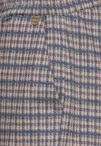 Blå och grädde rutigt tyg med en strukturerad väv, med en liten metallaccent vid fickan. Mönstret består av växlande rutor.