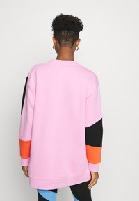 Sudadera rosa con acentos en negro y naranja, de manga larga, cuello redondo y corte relajado. Textura suave y detalles de diseño mínimos.