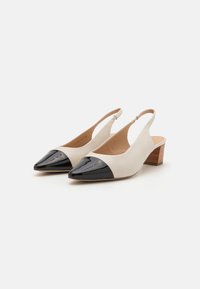 Slingback-sko med overdel i beige lær og spiss tå i svart lakklær. Har en lav trehæls design og åpen bak.