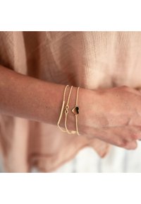 Aukso apyrankių rinkinys, kuriame yra trys grandinėlės: viena su begalybės simboliu, viena tekstūruota ir viena su juodu širdelės akcentu.