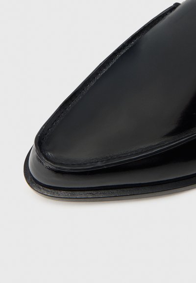Μαύρο δερμάτινο παπούτσι με μυτερή μύτη, λεία υφή και ορατή ραφή κατά μήκος της άκρης. Μινιμαλιστικός σχεδιασμός με ελαφριά λάμψη.