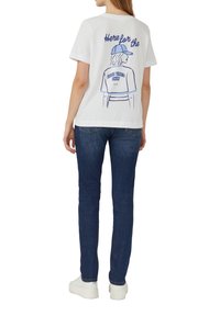 T-shirt en coton blanc avec un design graphique bleu au dos, sur lequel est inscrit "Ici pour le bon temps seulement" avec une figure stylisée.