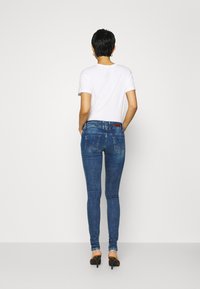 Blå tajta jeans i denim med medelhög midja, bakfickor med sömnadsdetaljer och en slät yta. Kombineras med en vit skjorta.
