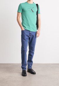 Grön bomullströja med svart CK-logotyp, ihop med blå jeans. Svarta loafers fulländar outfiten. Minimalistisk design, avslappnad passform.