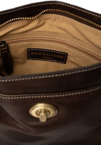 Interno di una borsa in pelle marrone caratterizzato da una texture liscia, rivestimento in tessuto beige, cerniera dorata e un'etichetta con la scritta "RE:DESIGNED EST 2003."