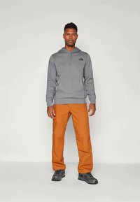 Γκρι φούτερ με κουκούλα και κορδόνι, διακοσμημένο με μαύρο λογότυπο, συνδυασμένο με πορτοκαλί παντελόνια cargo και μαύρες μπότες πεζοπορίας. Στάνταρ εφαρμογή και καθημερινός σχεδιασμός.