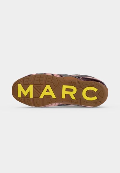 Semelle d'une basket avec une bande de roulement marron et de grandes lettres jaunes formant "MARC" en bas.