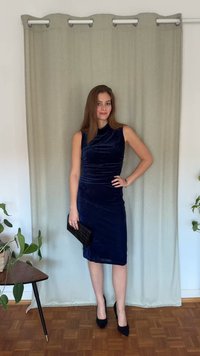 Granatowa aksamitna sukienka bez rękawów, dopasowana, z marszczeniami. Połączona z czarną kopertówką i wysokimi obcasami.