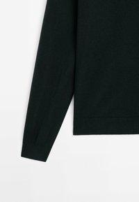 Donkergroene trui met lange mouwen, geribde manchetten en een gladde brei textuur. Geen zichtbare patronen of hardwaredetails.