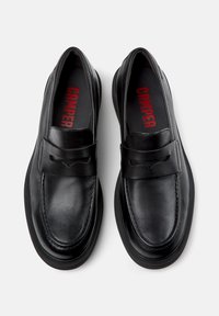 Pair of black leather slip-on loafers with rounded toes and "Camper" branding on the insoles, shown from above on a white background.