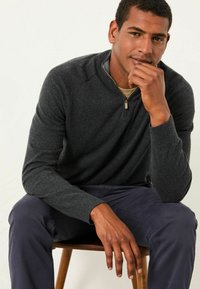 Dunkelgrauer Pullover mit einem Viertel-Reißverschluss-Kragen und gerippten Bündchen, kombiniert mit navyblauen Hosen. Glatte Textur, lässiges Design.