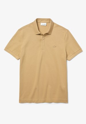Beżowa koszulka polo Lacoste wykonana z bawełny. Posiada ryżowy kołnierzyk, zapięcie na trzy guziki oraz tonowane haftowane logo na piersi.