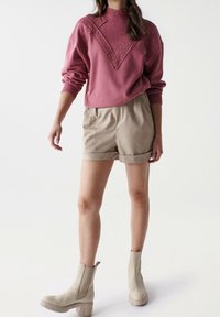 Sudadera rosa con detalles de encaje en el escote, combinada con pantalones cortos beige y botas beige hasta los tobillos con suela gruesa.