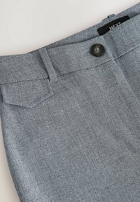 Pantalon gris texturé avec fermeture à bouton et passants pour ceinture, montrant la partie supérieure avant et un petit détail de poche.