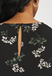 Zwarte stof met een bloemenprint van witte bloemen en groene bladeren. Heeft een keyhole-opening aan de achterkant met een zwarte knoopdetail.