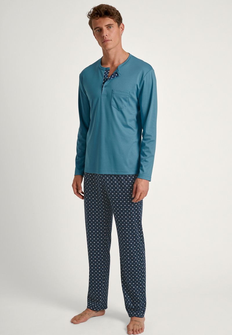 Turquoise langwerpige top met een zak en knoopsluiting; gecombineerd met navy broek met een wit vierkant patroon. Zachte stof.