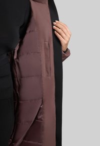 Chaqueta acolchada con un exterior negro y un interior burdeos. Presenta una textura suave, costuras visibles y un bolsillo lateral interior.