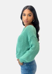 Jasnozielony sweter dziany o luźnym kroju, z dekoltem w serek i długimi rękawami, zestawiony z niebieskimi dżinsami. Miękka, teksturowana tkanina o swobodnym stylu.