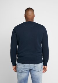 Marineblauwe gebreide trui met lange mouwen en ronde hals. Gestructureerd patroon, getailleerde taille en geribbelde manchetten. Achteraanzicht weergegeven.