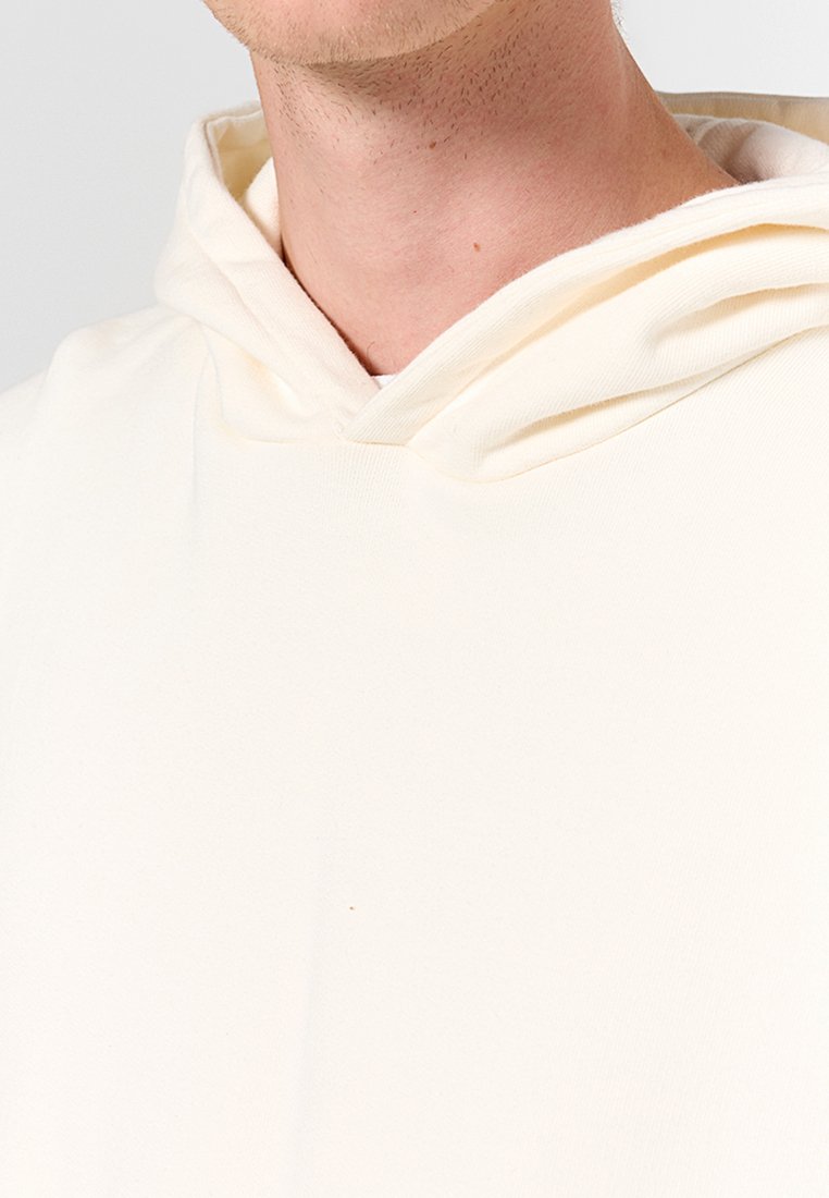 Pullover-Hoodie aus weichem Creme-Stoff, mit einer Kordelzugkapuze und glatter Textur, sowie einer Nahtdetail am Hals.