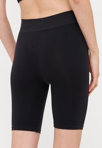 Black stretchy bike shorts with a smooth texture, mid-rise waistband, and hem falling just above the knee. Seamless construction details.