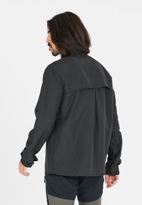Langsleeve zwart shirt met eenRelaxed fit, rugpas ontwerp, knoopmanchetten en een gladde textuur, gecombineerd met bijpassende donkere shorts.