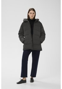 Szara pikowana kurtka puchowa z kapturem, zapinana na suwak z przodu. Do niej ciemnoniebieskie szerokie dżinsy i czarne buty.