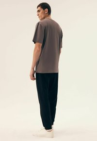 Szary t-shirt z krótkim rękawem o luźnym kroju, zestawiony z czarnymi spodniami i białymi trampkami. Gładka faktura, prosty design i minimalne detale.