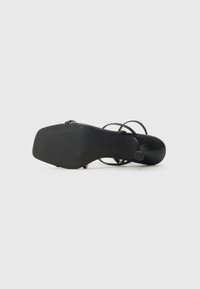 Sandal de salto alto preto com tiras finas. Parte superior em couro liso e sola em borracha texturizada. Apresenta uma tira traseira para segurança.