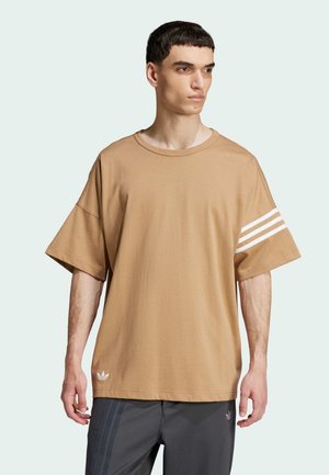 T-shirt oversize marrone in tessuto morbido, con tre strisce bianche su una manica e un piccolo logo sull'orlo. Maniche corte e larghe.
