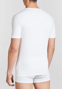 Camicia bianca a maniche corte realizzata in tessuto liscio, con scollatura tonda e vestibilità aderente. Indossata con pantaloni corti bianchi abbinati.