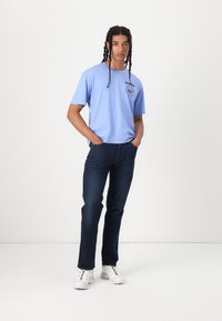 Light blue cotton t-shirt with short sleeves and a round neckline, paired with dark denim jeans and white sneakers. Logo on the chest.