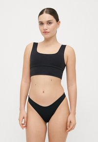 Black bikini set features a square-neck crop top and low-rise bottom. Made from smooth fabric with a minimalist design and subtle stitching.