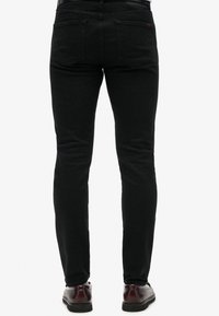 Czarne dżinsy o wąskim kroju, z tylnymi kieszeniami i szlufkami na pasek. Materiał ma gładką teksturę i subtelny połysk.