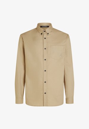 Hosszú ujjú bézs ing, gombos nyakkal, fekete gombokkal, mellzsebbel és egy diszkrét hímzett logóval a zseben.