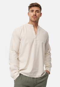 Camicia a maniche lunghe beige chiaro con collo henley abbottonato, realizzata in un tessuto testurizzato. La camicia ha una vestibilità rilassata e un orlo arrotondato.