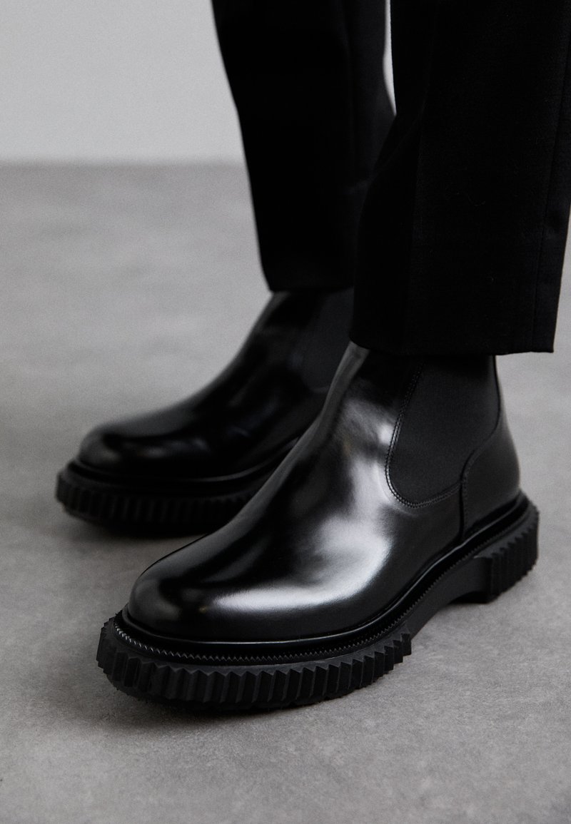 Botas Chelsea de cuero negro con un acabado suave, paneles laterales elásticos y una suela de goma gruesa y texturizada que presenta un patrón de banda de rodadura resistente.