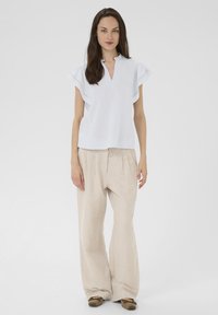 Blusa bianca a maniche corte con scollatura a V e dettagli a balze, abbinata a pantaloni beige a gamba larga realizzati in tessuto texture.