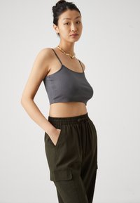 Grå ribbet cropped topp med tynne stropper, sammen med olivengrønne cargo-bukser med elastisk liv, som har sidelommer og en strukturert overflate.