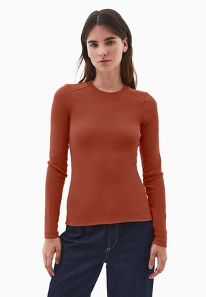 Top de manga larga acanalado en color óxido, con un escote redondo y un diseño ajustado, combinado con jeans de mezclilla azul oscuro.