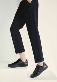 Bordowe skórzane trampki z tłoczonym wzorem krokodyla, czarne sznurowadła i złote dodatki, w połączeniu z dopasowanymi czarnymi spodniami.