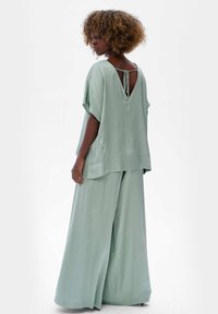 Lichtgroene, vloeiende blouse met een V-hals en een strikdetail op de rug, gecombineerd met wijde broekspijpen in dezelfde kleur en materiaal. Glad textuur.