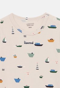 Ελαφρύ μπεζ οργανικό βαμβακερό t-shirt με εκτυπώσεις ναυτικής θεματολογίας που απεικονίζου ν βάρκες, φάρους και σωσίβια σε διάφορα χρώματα. Στρογγυλή λαιμόκοψη.