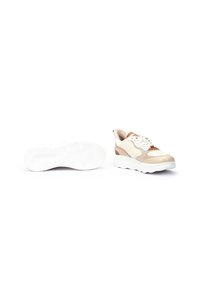 Une paire de baskets beige et blanche avec des semelles blanches épaisses, l'une montrant le dessus, l'autre montrant la semelle sur un fond blanc.