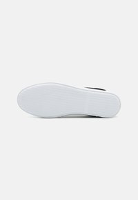 Suela de zapato de goma blanca con una superficie texturizada y surcos sutiles. Presenta un diseño superior negro y amortiguación para mayor comodidad.